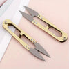 A pair of gold-colored U-shape sewing scissors with sharp blades resting on a light pink surface.
