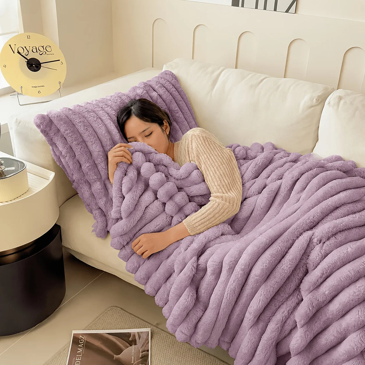 A woman is relaxing on a white sofa covered with a purple fleece throw blanket.