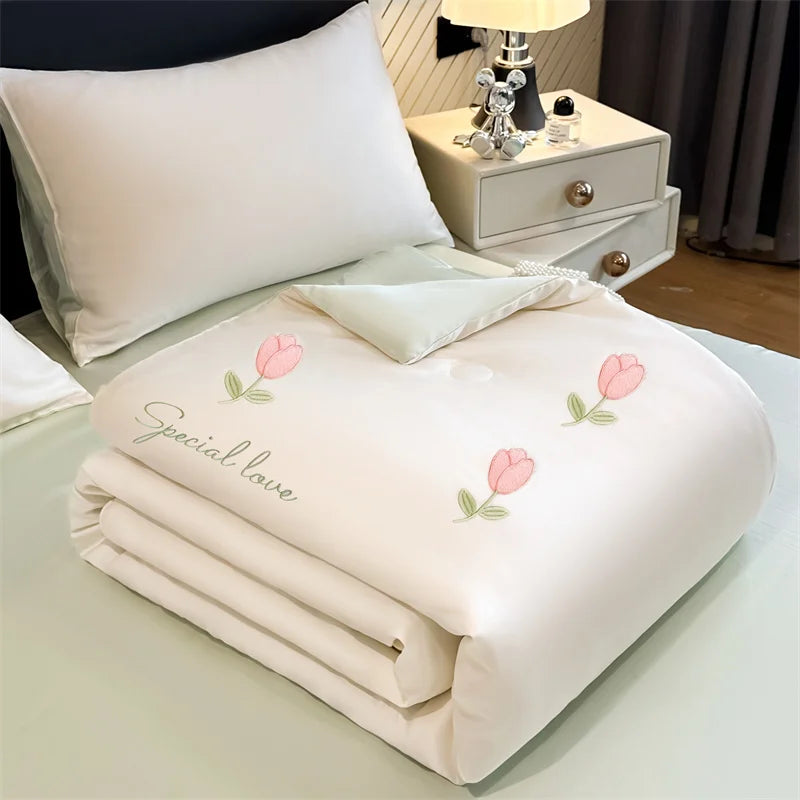 A white embroidered quilt with pink tulip designs is folded on a light green surface.