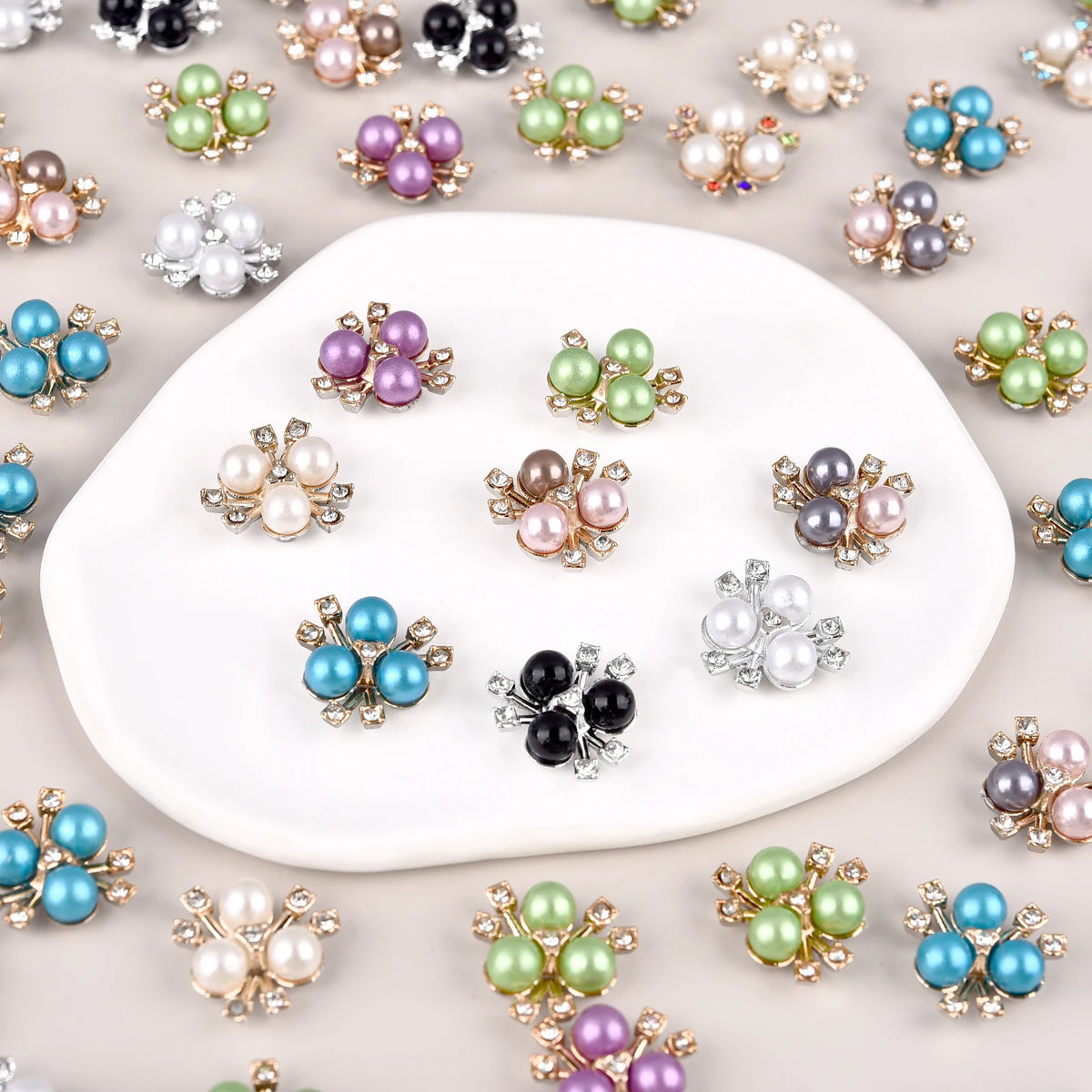 A collection of flower-shaped resin button rhinestones in various shades of pink, green, blue, and purple scattered on a whit