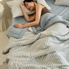 A woman rests on a bed covered with a striped light blue and white quilt.