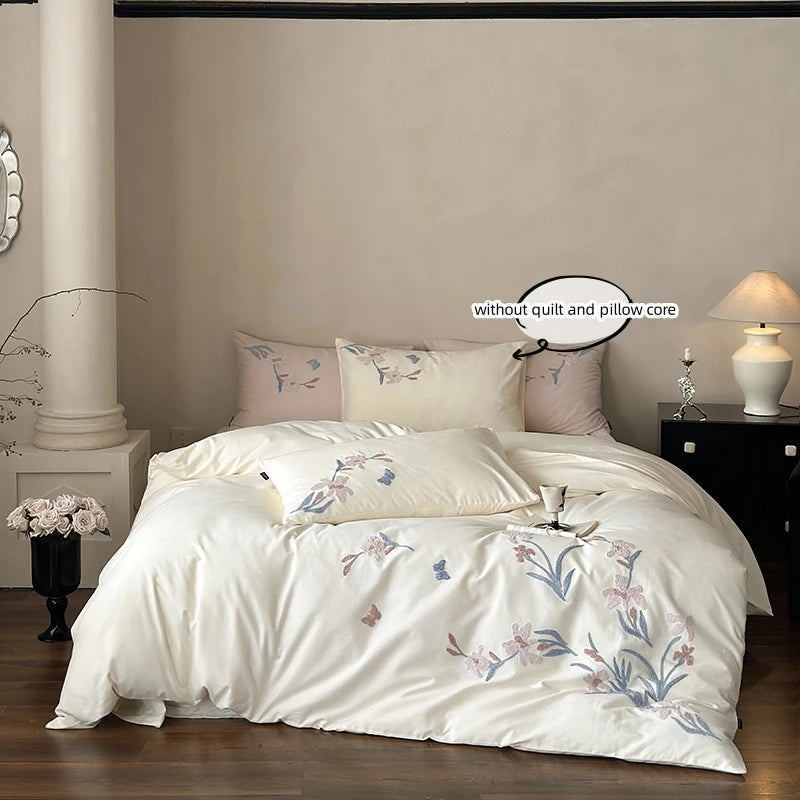 A white embroidered orchid duvet cover set displayed on a bed with a dark wood nightstand.