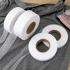 Rolls of white double-sided heat-resistant interlining tape laid on a gray fabric.