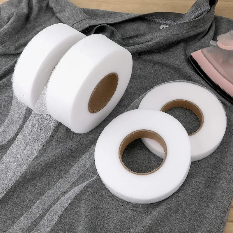 Rolls of white double-sided heat-resistant interlining tape laid on a gray fabric.