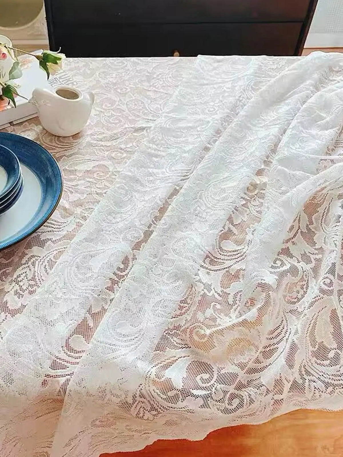 A white vintage lace tablecloth draped over a wooden table with blue plates and floral accents.