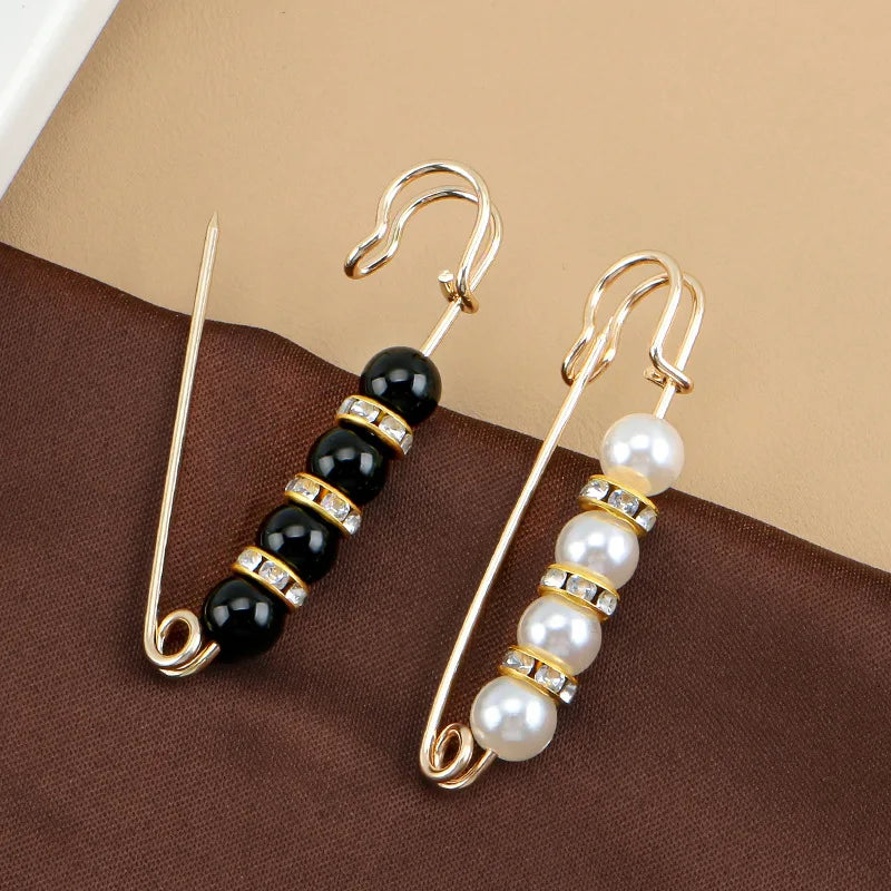 Gold-toned adjustable pearl earrings with black beads displayed on a brown fabric.