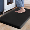 A person's feet are standing on a black anti-fatigue PVC kitchen mat placed on a light wooden floor near a white appliance.
