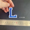 A hand holds a blue alphabet embroidery patch shaped like the letter L, measured at 5.1 by 4.1 cm.