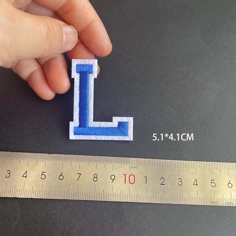 A hand holds a blue alphabet embroidery patch shaped like the letter L, measured at 5.1 by 4.1 cm.