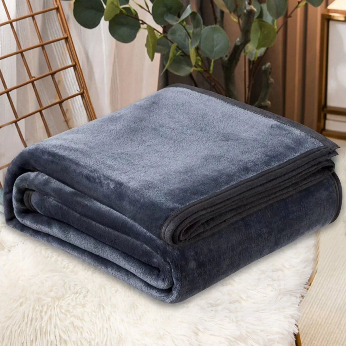 A dark blue cozy coral fleece throw blanket folded neatly on a white fluffy surface.