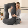 A woman is lying down, embracing a gray J-shaped ergonomic maternity pillow on a white bed.