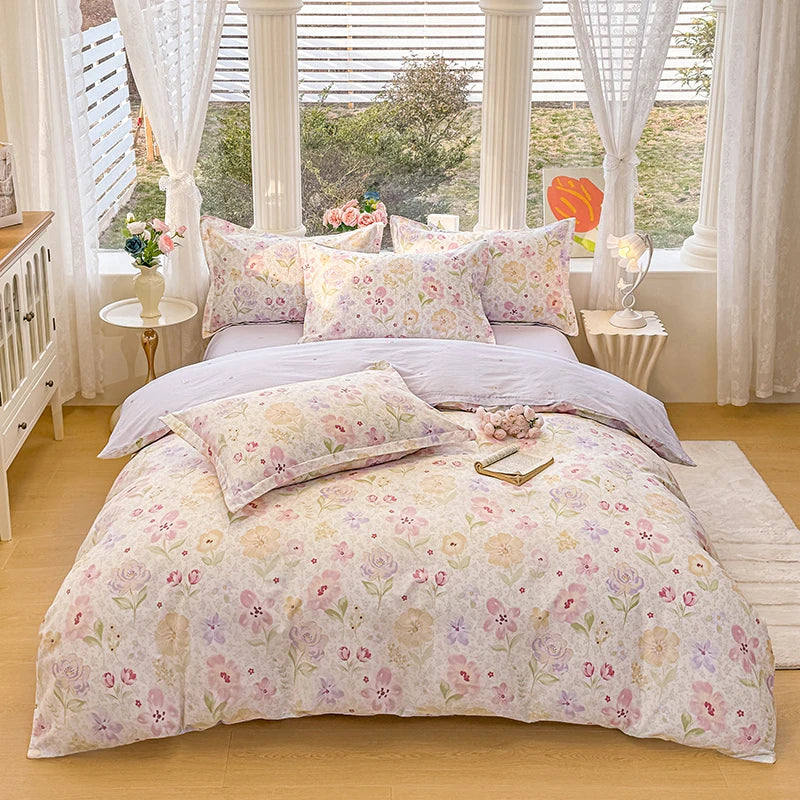 A light pink floral duvet cover and pillow set displayed on a bed with white curtains and wooden furniture.
