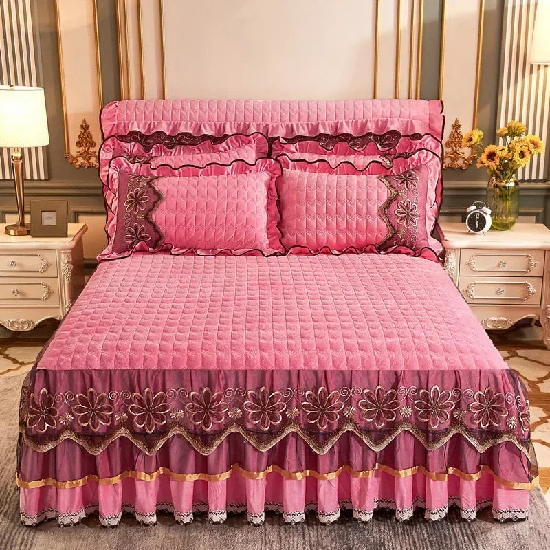 Pink quilted bed skirt with lace trim and embroidery on a pink quilted bed.