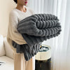 A person is holding a large, gray, fluffy plush winter blanket against their chest.