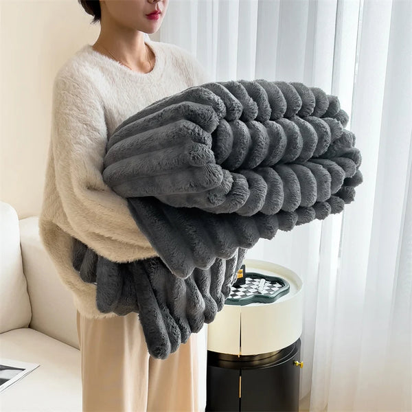 A person is holding a large, gray, fluffy plush winter blanket against their chest.
