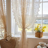 A sheer lace curtain in beige hangs over a window, decorated with a beaded phoenix tail design.