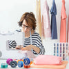 A woman is using a clear sewing machine bobbin and thread on a white sewing machine, with various pink and blue fabric pieces