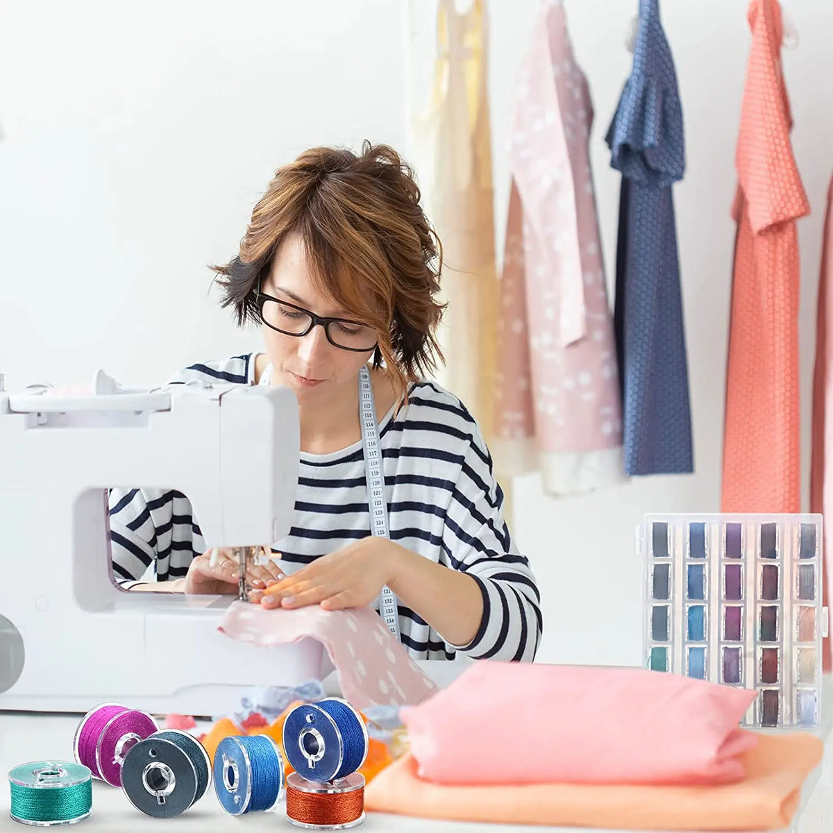 A woman is using a clear sewing machine bobbin and thread on a white sewing machine, with various pink and blue fabric pieces