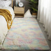 A fluffy rug with pastel pink, blue, and yellow hues placed on a wooden floor next to a bed.