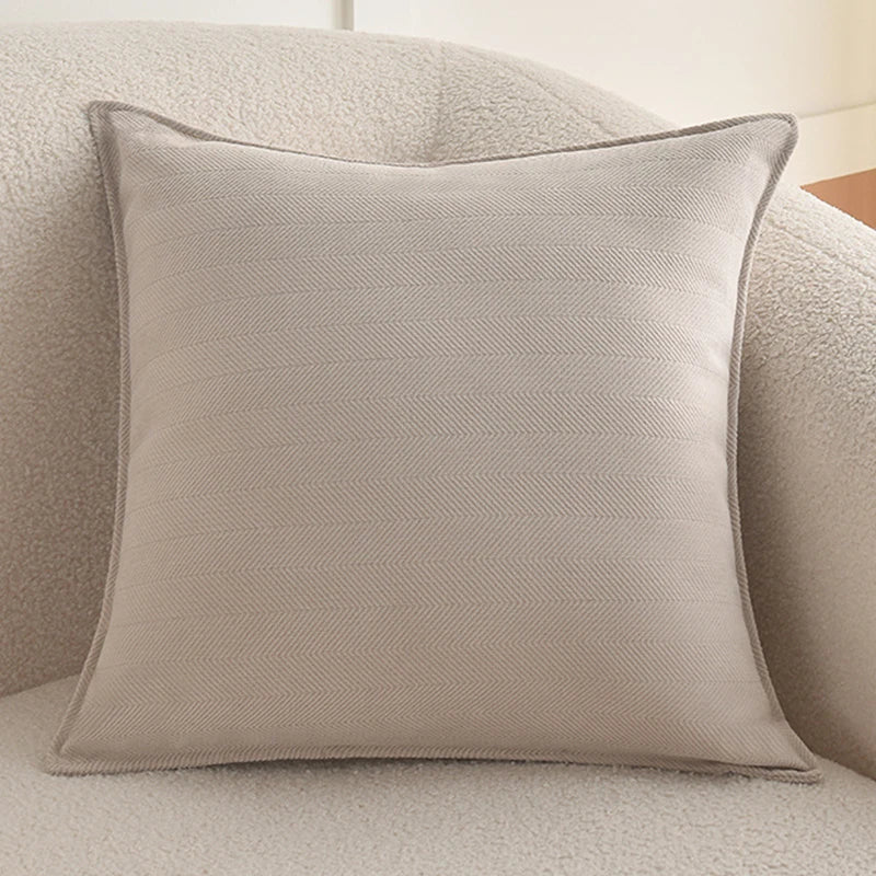 A light beige luxury chenille throw pillow cover resting on a soft, textured sofa.