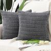 A set of two dark gray knitted textured throw pillows resting on a white textured fabric.