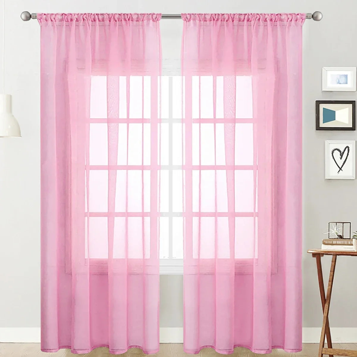 Pink sheer curtain with rod pocket hanging over a white window.