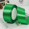 A roll of vibrant green satin ribbon lying on a sheet of paper.