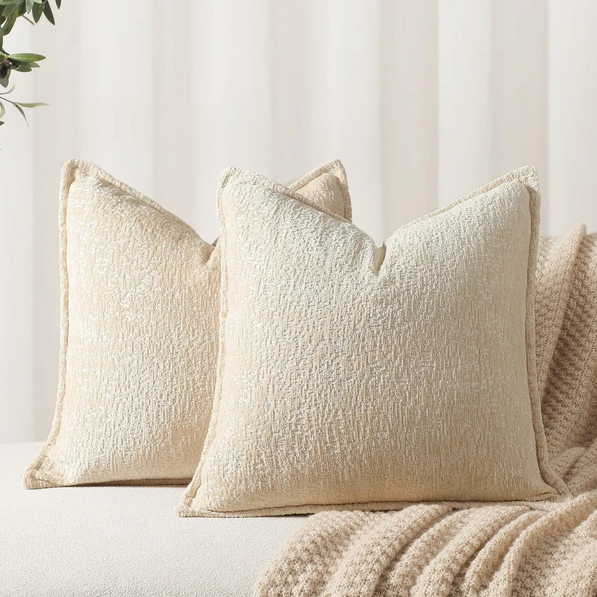 A close-up of a cream colored chenille throw pillow resting on a light beige fabric.