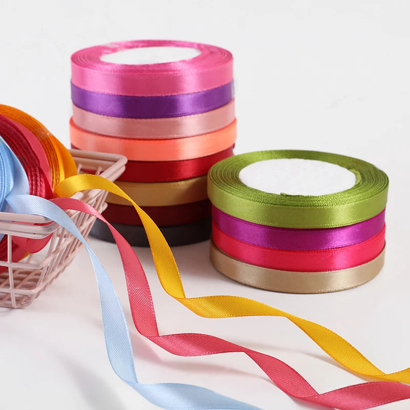 A collection of satin ribbons in assorted colors, including pink, purple, orange, and yellow, are rolled on a white backgroun