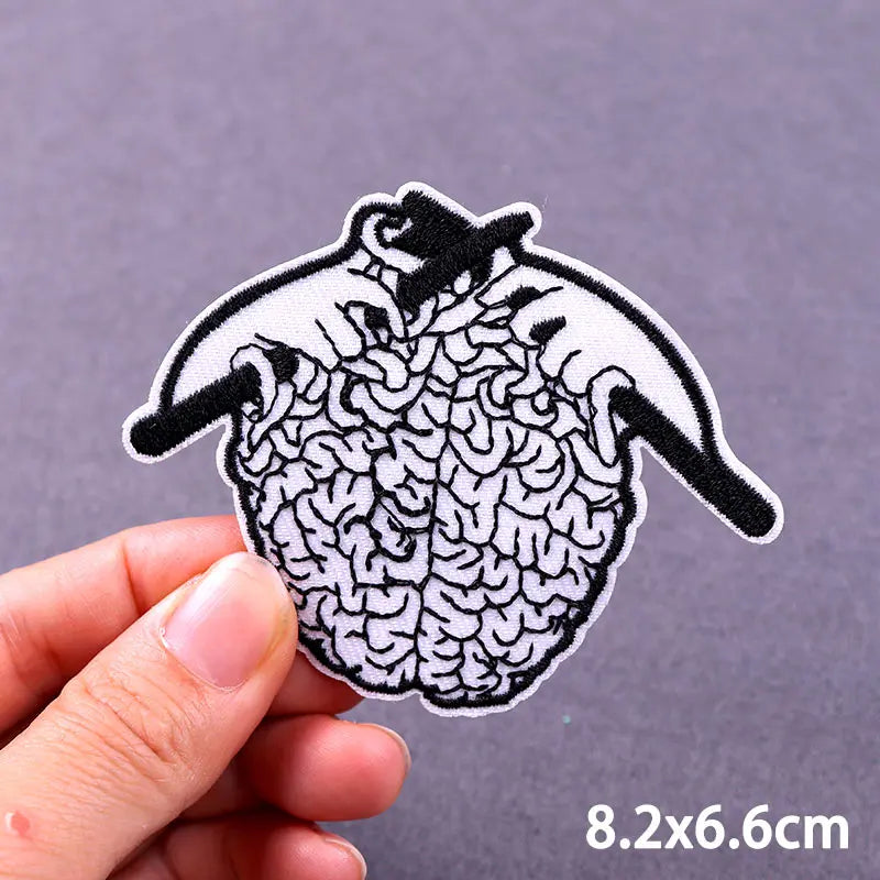 Black and white embroidered skull iron-on patch with a detailed brain pattern on a hand