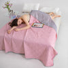 A woman is relaxing on a pink breathable cooling blanket with a purple throw, reading on her lap.