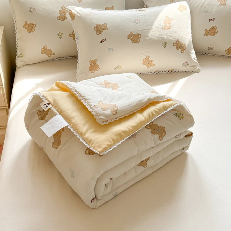 A stack of cream and yellow quilted blankets featuring small brown bear embroidery.