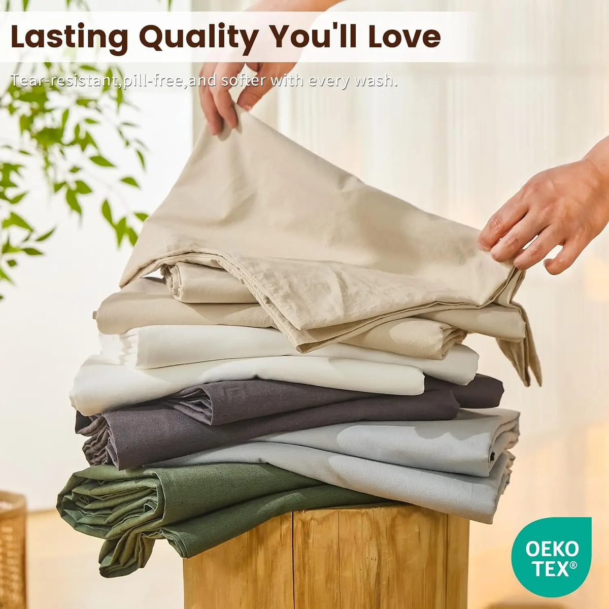 A stack of natural linen fabric in various shades of beige, gray, and green is being held by a hand.