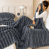 A dark gray, chunky fleece throw blanket is draped over a white sofa next to a lamp.
