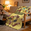 A yellow plush throw blanket featuring illustrations of Curious George and friends, draped over a wooden chair.