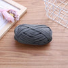 A ball of gray flat thread yarn lying on a wooden surface next to a white wire basket and some pink flowers.
