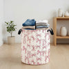 A beige canvas laundry basket filled with folded white and blue towels decorated with pink bow patterns.
