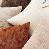 A collection of textured throw pillows in shades of beige, brown, and olive green.