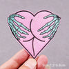 Pink heart shaped embroidered patch featuring green claw hands