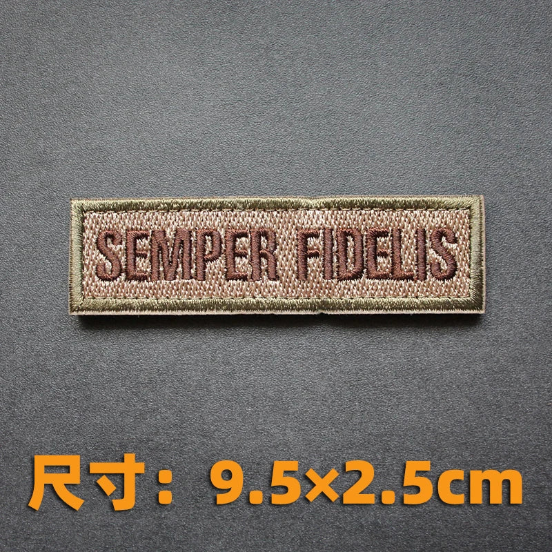 A brown embroidered badge with the text SEMPER FIDELIS on a dark gray background.