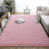 A fluffy pink rainbow plush area rug placed in a bright room with a sofa and indoor plants.