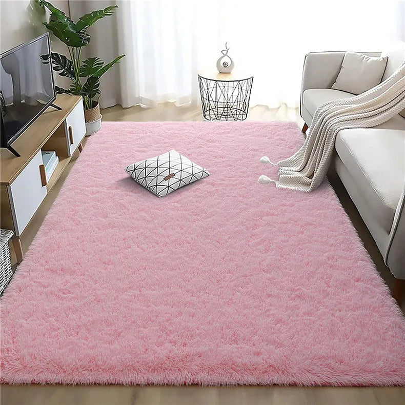 A fluffy pink rainbow plush area rug placed in a bright room with a sofa and indoor plants.