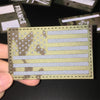 A close-up of a tactical patch featuring the American flag design in camouflage and light gray stripes.