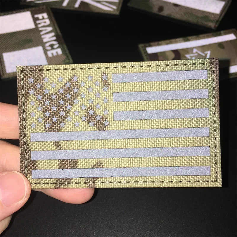 A close-up of a tactical patch featuring the American flag design in camouflage and light gray stripes.