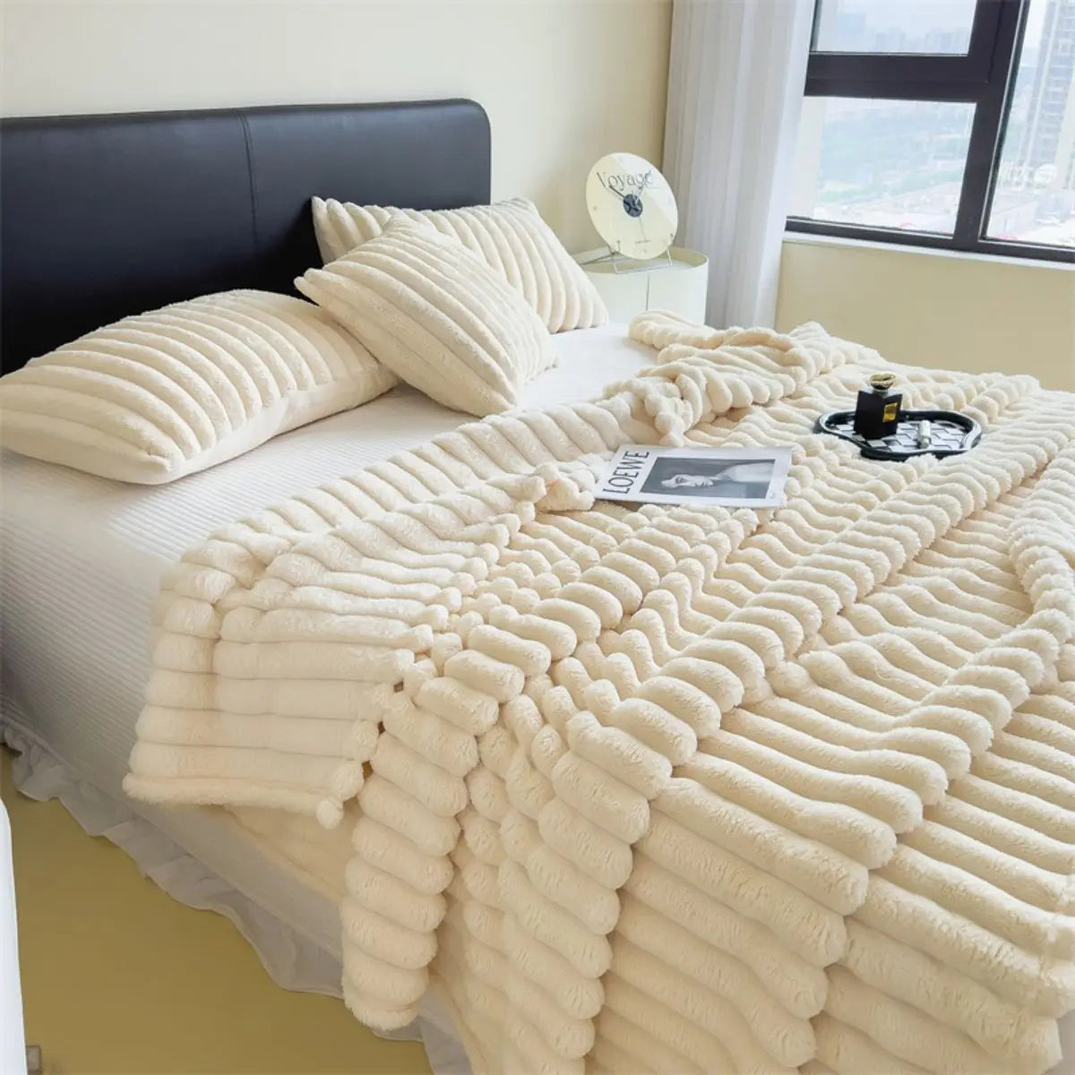 A thick, cream-colored cozy blanket with a ribbed texture is draped over a white bed.