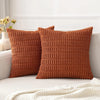 A close-up of two textured, rust-colored corduroy throw pillows resting on a light sofa.