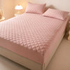 A pink quilted mattress protector is displayed on a bed with matching pillows and a bedside lamp.