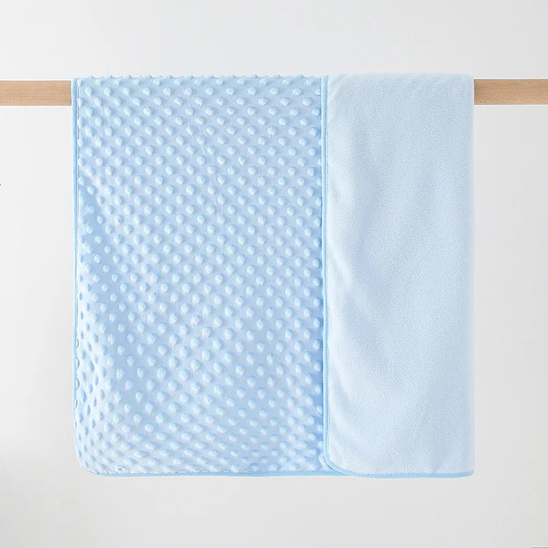 Light blue fleece swaddle blanket with a textured pattern hanging on a wooden rod.