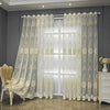 White sheer curtain with beige embroidery and punched-hole design hanging in a modern room.