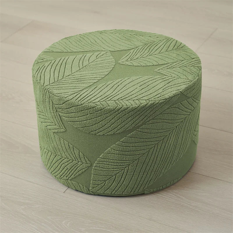 A round, olive green jacquard ottoman footrest slipcover with a textured leaf pattern.